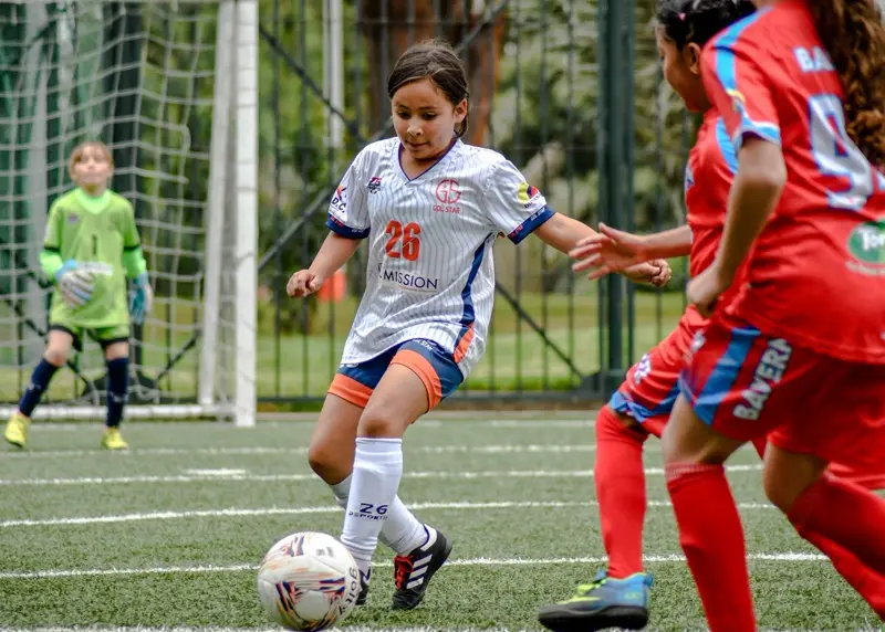 A young player dribbles past a defender in front of goal