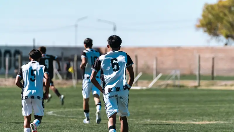 Youth players in striped kits walk across a sunny pitch