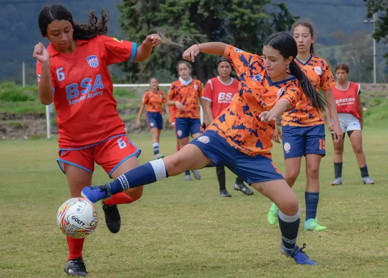 Two youth players chase the ball on a grass field